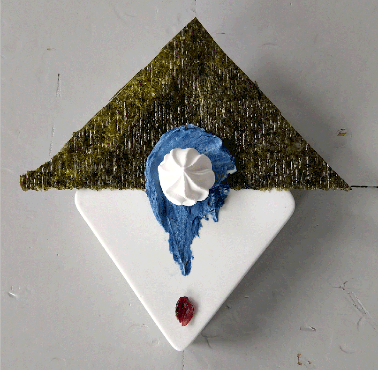 ALKANARA - Uma sobremesa artística com uma cobertura triangular verde, cobertura azul, uma colherada de chantilly e uma baga vermelha num prato branco. - ©Celestial Bodies