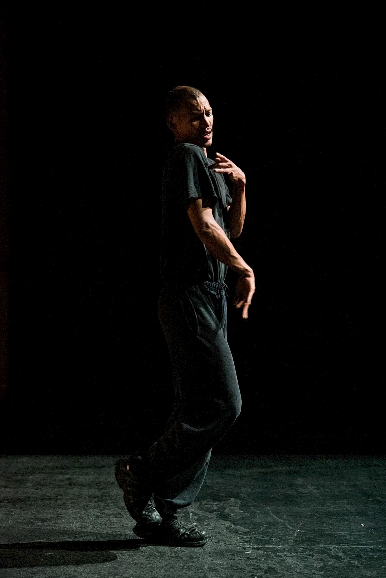 ALKANARA - A person dressed in black sportswear poses dramatically against a dark background, displaying expressive body movements. - ©José Caldeira