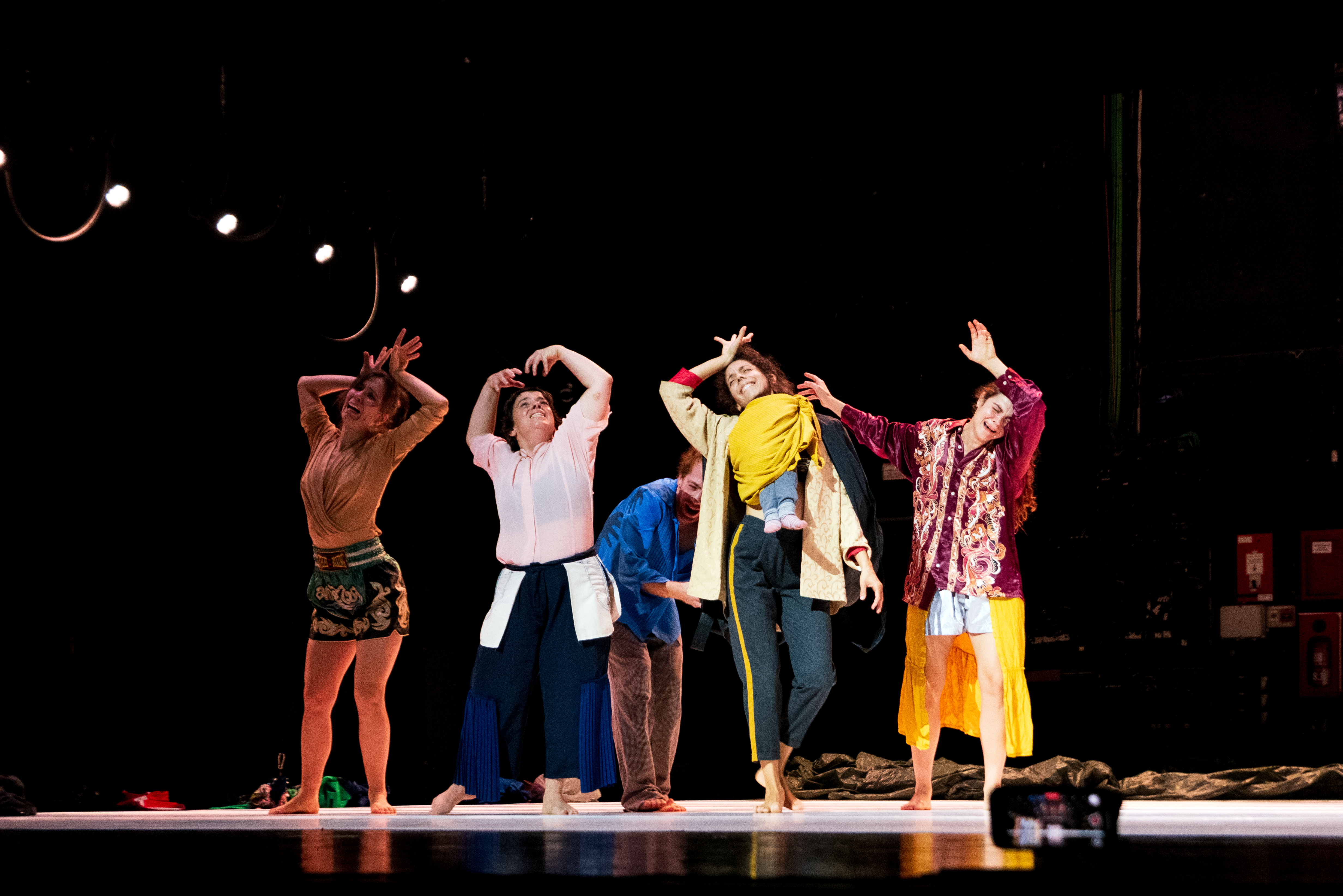 © Walesca Timmen Five people perform on stage, each striking different expressive poses with raised arms and distinct outfits under stage lights. - Walesca Timmen